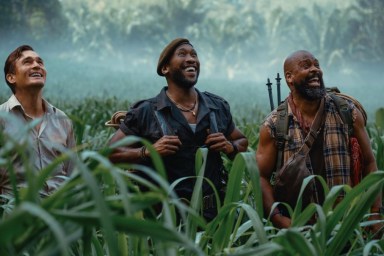 Three men look up while standing in a field.
